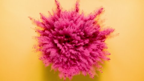 Dark pink colored powder exploding towards camera in close up and super slow-motion, golden yellow background
