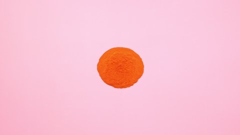 Orange colored powder exploding towards camera in close up and super slow-motion, pink background