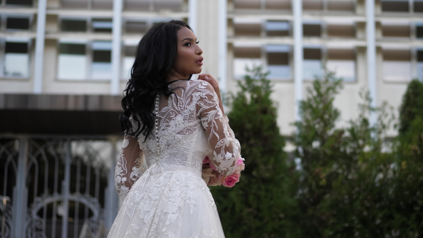 pretty African american lady in gorgeous wedding dress with laces on street against hotel side view slow motion