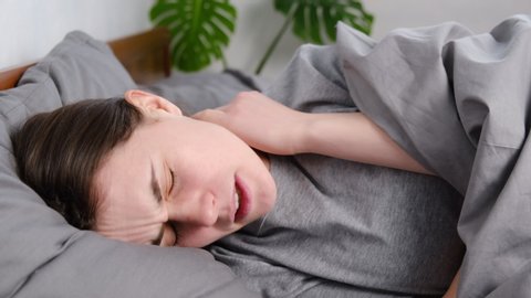 Tired upset young woman massage tense neck muscles lying in bed, stress relief, exhausted girl suffering from pain, feeling physics discomfort. Fibromyalgia concept