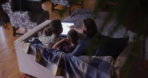  Social distancing and self isolation in quarantine lockdown. Caucasian couple and their two young sons at home in the living room in the evening, sitting on a sofa together looking at a laptop