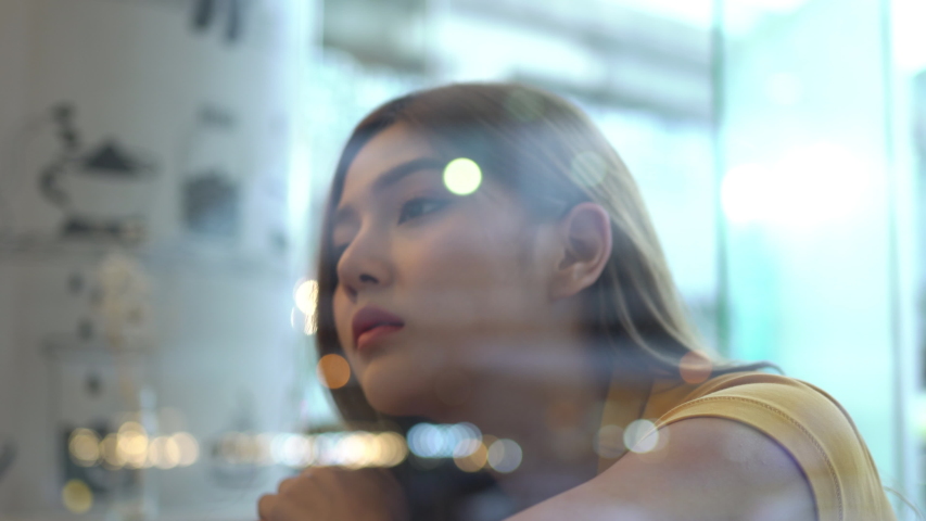 4K Depressed Young beautiful Asian woman teenage girl sitting by the window in cafe at night. Lonely sad woman looking away out of coffee shop window to city street and night lights with sadness eyes. Royalty-Free Stock Footage #1048690525