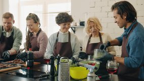 Multi-racial group of cooking class students in aprons are making meals in kitchen talking to chef enjoying activity. Hobby, cookery and communication concept. - Powered by Shutterstock - Get 15% off with code: PIKWIZARD15