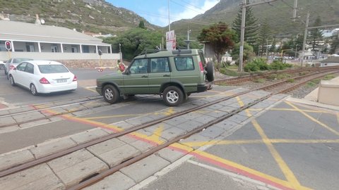KALK BAY, SOUTH AFRICA, CIRCA MARCH 2020, African man lets down train crossing after illegally opening it and receives tip from car driver, another vehicle stopped across train line, distant train