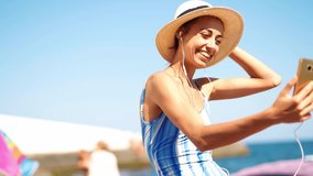 joyful beautiful woman in swimwear and straw hat making selfie or video call, smiling to camera, enjoying beach summer vacation on resort. Tourism and travel concept.