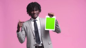 African american businessman showing digital tablet and like sign isolated on pink
