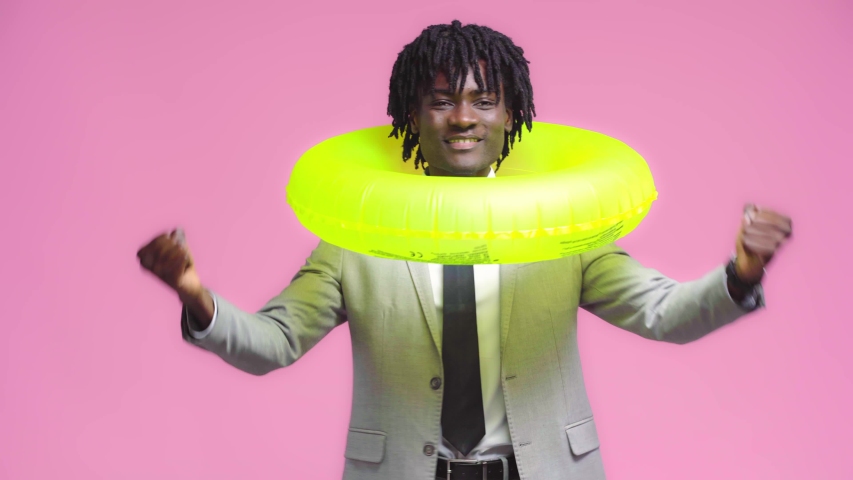 Happy african american businessman with swim ring waving hand isolated on pink