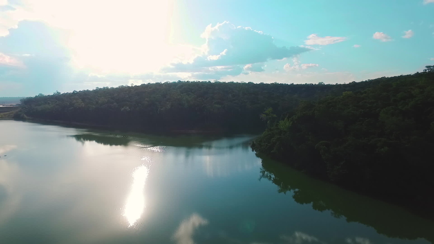 Black river with Amazon forest in the background, silhouetted against the light. Blue skies and clouds help compose the scene of tranquility and peace.