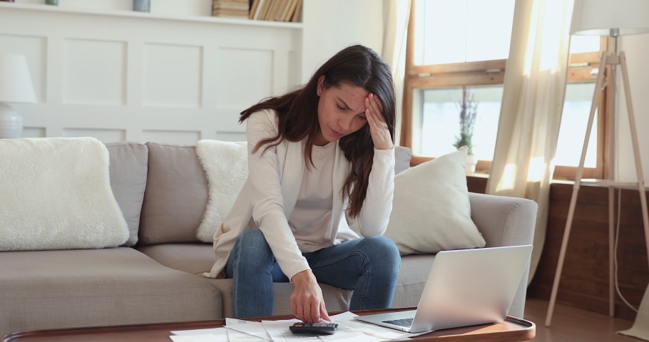 Upset young woman feeling stressed about financial debt checking bills at home. Frustrated lady doing paperwork sitting on sofa thinking of unpaid tax, bank loan, money problem or bankruptcy concept. Royalty-Free Stock Footage #1048713304