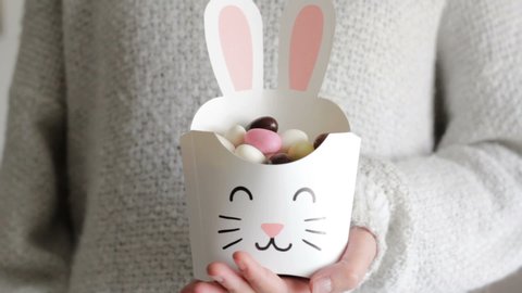 Woman holding a treat box in shape of bunny and eating easter almonds from it