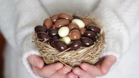 Woman's hands giving easter chocolate eggs in nest