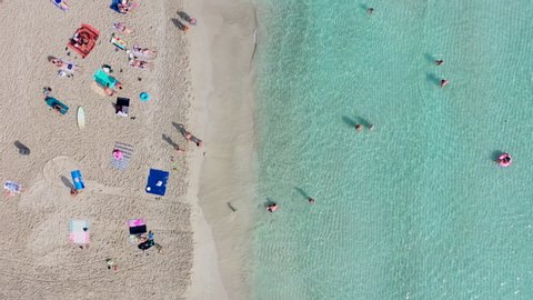 Top down aerial shot of a beautiful sandy beach. Camera moves along the shore, various bathers and swimmers enjoy the beach