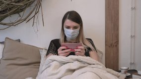 Girl in medical mask on home quarantine plays mobile games