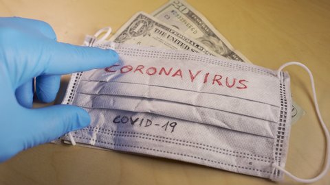 Hands with blue medical gloves putting a respirator mask with the word coronavirus on top of dollar bills.Global stock markets financial crisis and crash caused by the coronavirus outbreak