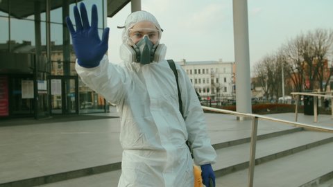 Man, worker disinfects against coronavirus, makes stop sign with hand, saying no, expressing restriction. Sanitary measures in public place during quarantine. Slow-mo