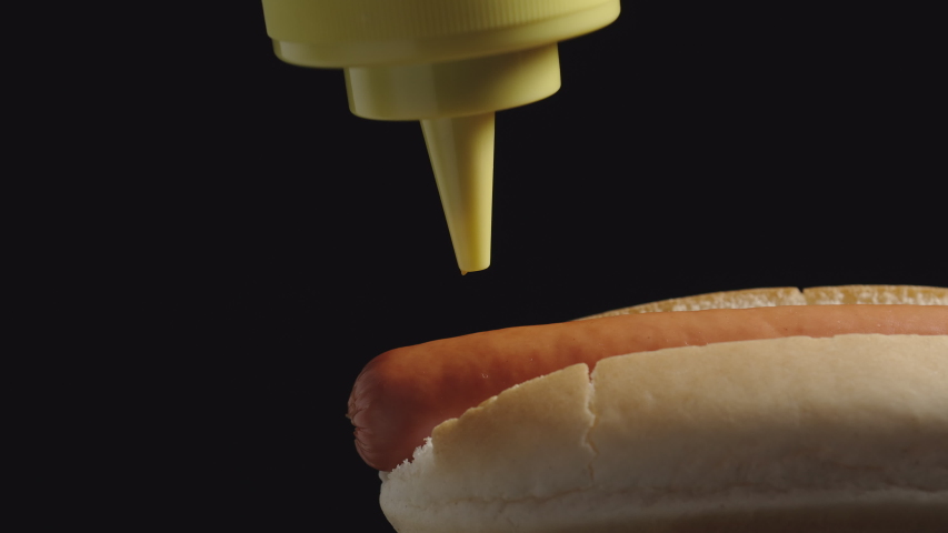 CLOSE UP: Yellow mustard sause poring on a hot dog with sausage from a bottle. Side View
