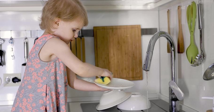 little girl washing dishes with sponge in kitchen sink at home