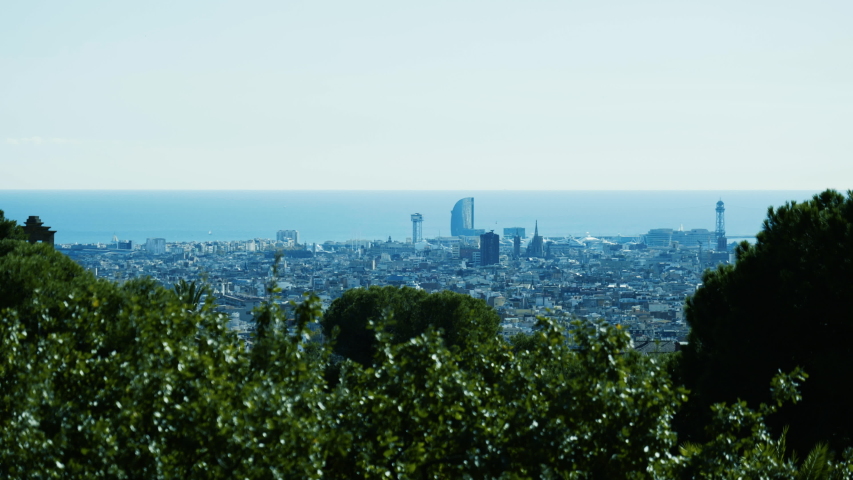 Wide view of beautiful cityscape of Barcelona with green nature in the foreground at a sunny day.