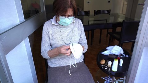 Europe, Italy, Milan - 70 year old lady with quarantine mask at home to protect herself from the epidemic n-cov19 Coronavirus makes domestic activity - sew and repair the mask anti-virus