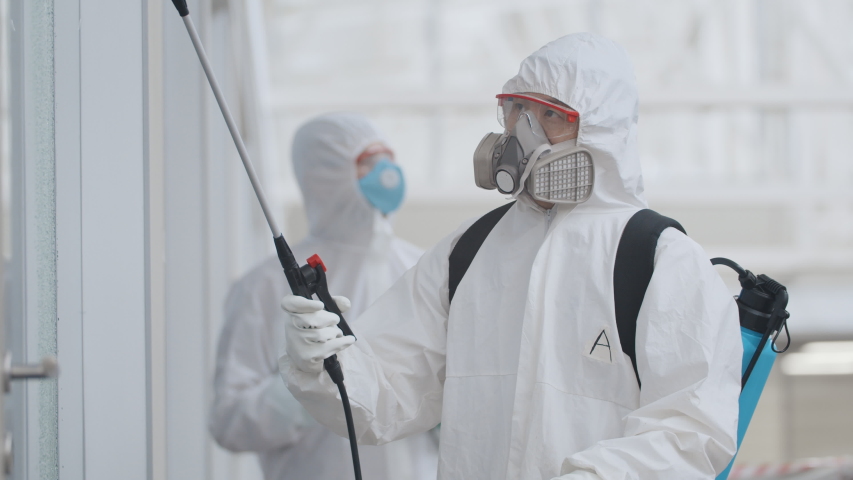 Covid-19 outbreak. People in protective suits spray disinfectant chemicals on walls of business center to prevent the spreading of the coronavirus. Scientists using chemicals to disinfect public place | Shutterstock HD Video #1048778053