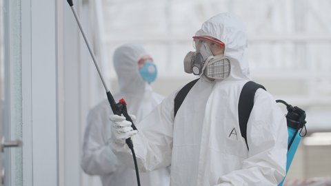 Covid-19 outbreak. People in protective suits spray disinfectant chemicals on walls of business center to prevent the spreading of the coronavirus. Scientists using chemicals to disinfect public place