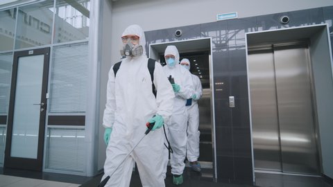 Covid-19 spreading. Group of scientists in protective wear and masks with special equipment disinfecting modern center fighting coronavirus. Team of disinfectors working in office building