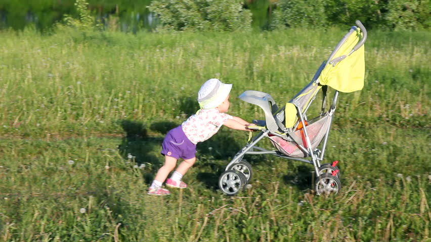 child pushes stroller on summer lawn