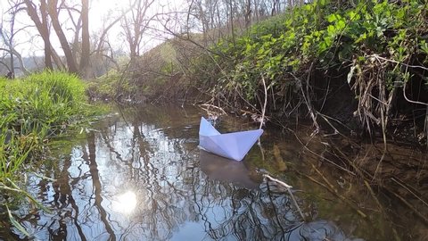 Girl launches paper boat. Spring water stream.