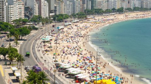 Aerial timelapse of the Copacabana beach in Rio de Janeiro, Brazil. View of the busy beach full of people and tents, the ocean and the buildings.