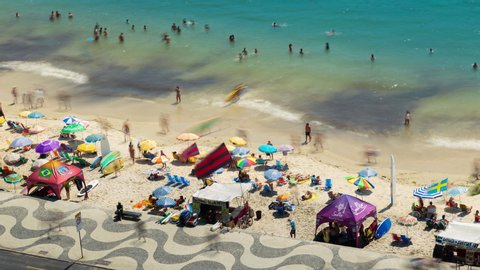 Rio de Janeiro, Brazil - February 25, 2020: Aerial timelapse of Copacabana street and walkway with traffic and people walking on the beach. View of the ocean, chairs, shops and swimmers 