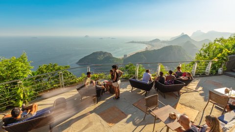 Rio de Janeiro, Brazil - March 11, 2020: Timelapse of crowded rooftop bar restaurant on top of Sugarloaf mountain. View of people drinking. Ocean, Copacabana and Ipanema beach in background.