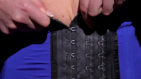This closeup video shows anonymous female hands putting on a tight corset waist trainer.
