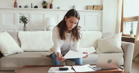 Serious young woman renter reviewing paperwork calculating taxes or household bills at home. Millennial lady counting mortgage loan rate, rent payment, managing finances to make savings concept.