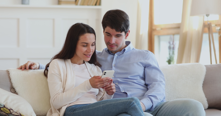 Excited young couple winning giveaway lottery prize in social media app online on smartphone. Happy euphoric millennial man and woman winners celebrating success holding mobile phone sitting on sofa. Royalty-Free Stock Footage #1048785430