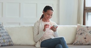 Millennial woman looking at smartphone surfing social media app. Smiling young lady customer texting mobile sms message at home. Happy female customer using smart phone technology sitting on couch