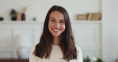 Cheerful pretty millennial woman looking at camera laughing with dental smile standing at home office indoors. Happy young beautiful lady close up portrait. White healthy teeth, dentistry concept