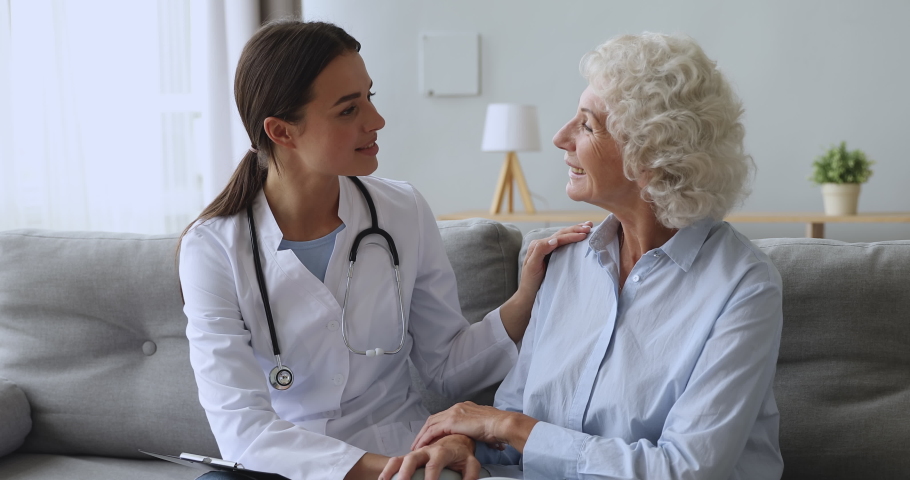 Happy older middle aged woman feeling thankful to young female therapist at home. Pleasant kind doctor general practitioner in uniform supporting retired patient, communicating during checkup visit. Royalty-Free Stock Footage #1048785508