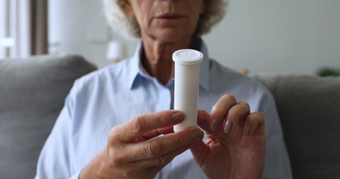 Close up middle aged woman holding plastic bottle with pills, reading prescription side. Older mature retired patient familiarizing with composition side effects, healthcare medicament concept.