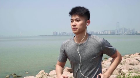 asian young man listening to music while running jogging outdoors in a seaside park
