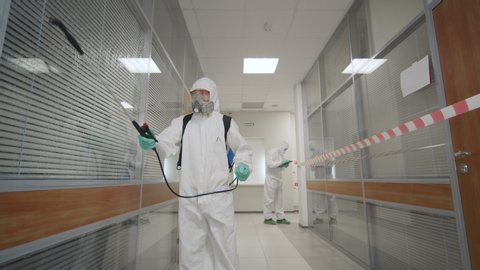 2019-ncov spreading, coronavirus outbreak. Team of virologists in protective coveralls and masks working in office building disinfecting rooms fighting against coronavirus spread.