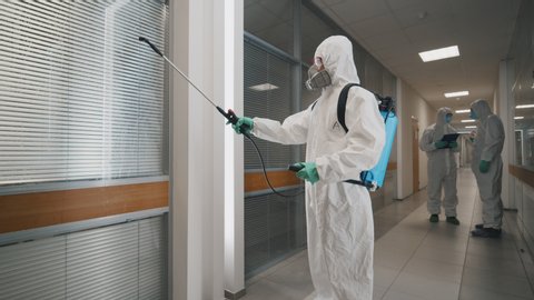 Covid-19 spreading. Workers in hazmat suits and respirator masks sprays disinfectant in office building as part of preventive measures against the spread of the coronavirus