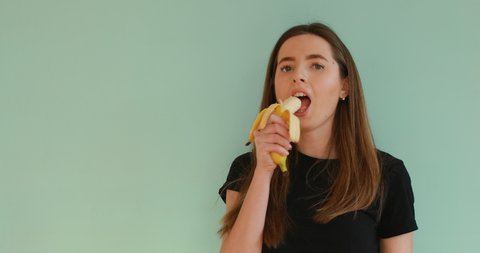 young brunette girl eating banana on turquoise background