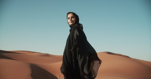 Young beautiful girl in traditional Abaya dress walks along the dunes in the desert of Dubai. 4K Slow Motion