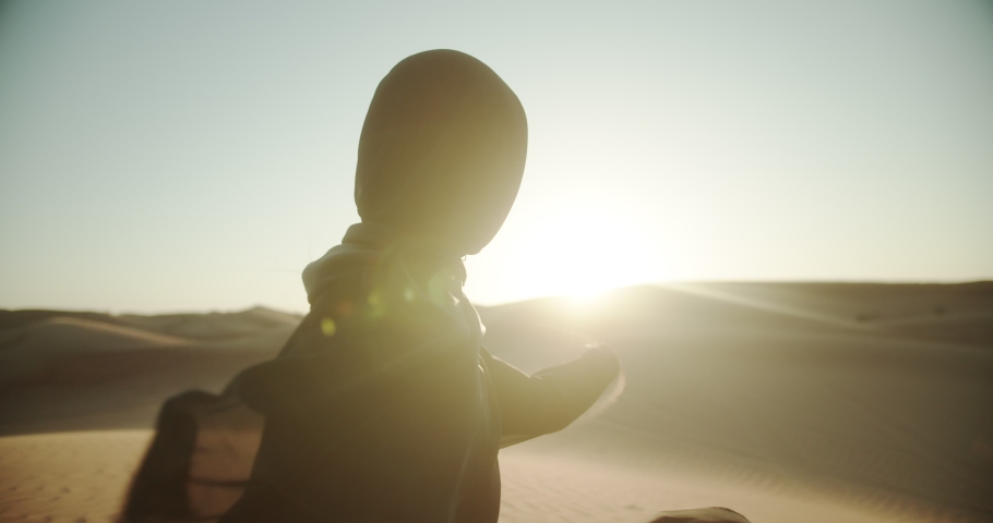 Arab girl in hijab and abaya in the desert at sunset holds sand in her hands. 4K Slow Motion Royalty-Free Stock Footage #1048799800