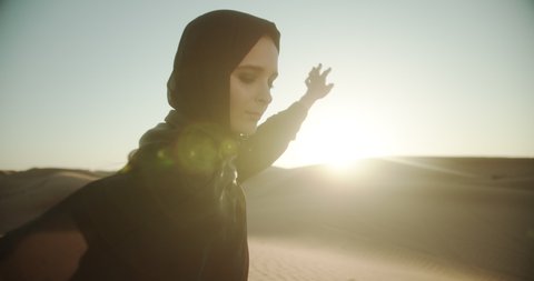 Arab girl in hijab and abaya in the desert at sunset holds sand in her hands. 4K Slow Motion