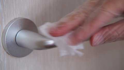 A hand wearing disposable rubber glove cleans door handle by alcohol slice