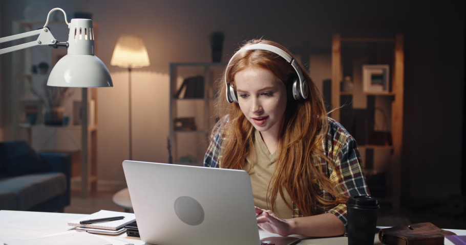 Positive redhead caucasian high school or university student listening to music in headphones and concetrating on work. Young freelancer enjoying remote job in laptop 4k footage Royalty-Free Stock Footage #1048803325