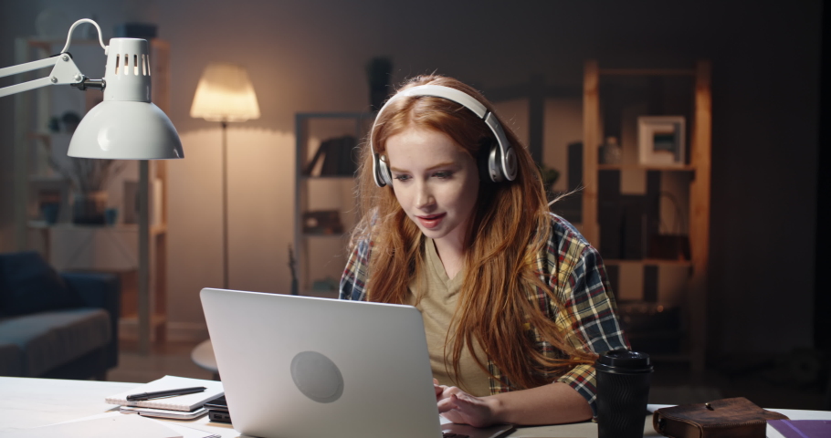 Positive redhead caucasian high school or university student listening to music in headphones and concetrating on work. Young freelancer enjoying remote job in laptop 4k footage Royalty-Free Stock Footage #1048803325