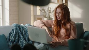 Attractive caucasian redhead model sitting on couch looking at laptop screen, having video chat online, participating in webinar, having a conference - communication, connection concept 4k footage - Powered by Shutterstock - Get 15% off with code: PIKWIZARD15