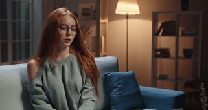 Pretty caucasian redhead girl sitting on coach looking at laptop, having a videochat or online tutorial, recording an internet vlog, cute model looking at webcamera and talking 4k footage